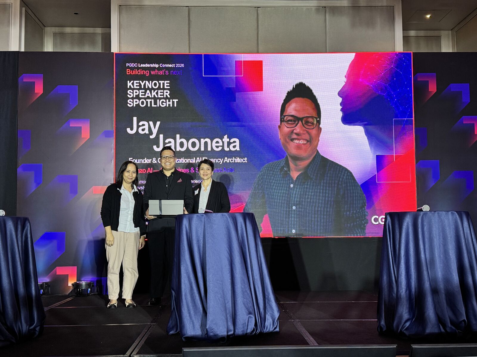 Jay Jaboneta with two organizers in front of the Keynote Speaker Spotlight screen at CGI's PGDC Leadership Connect 2026